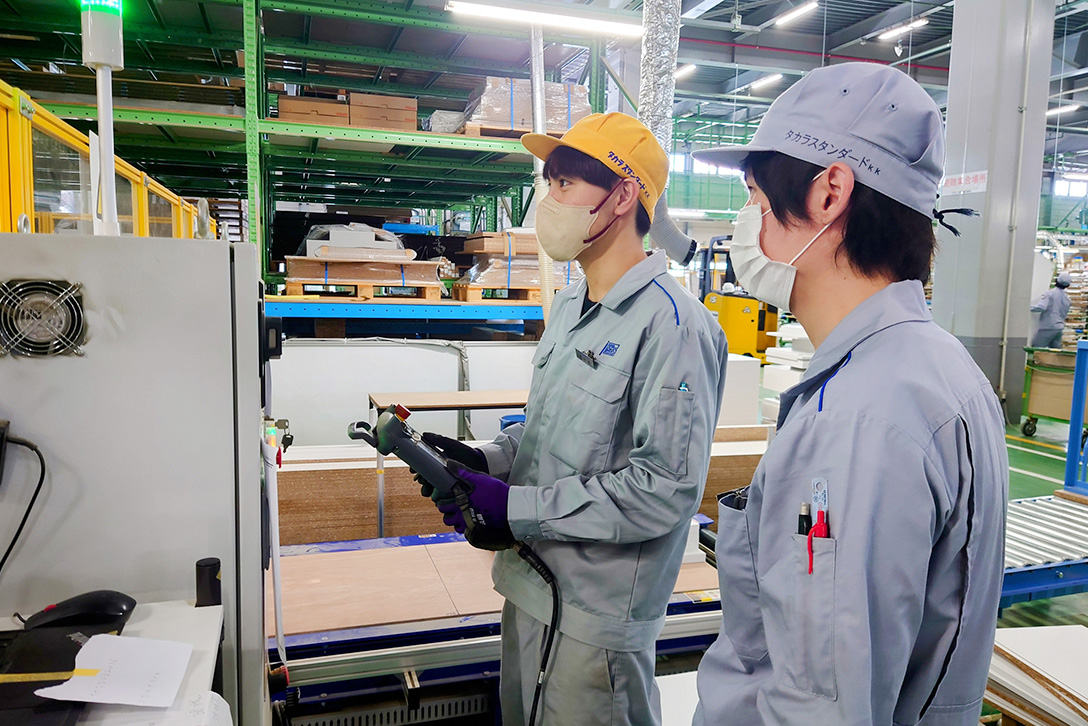 ロボット設備の操作方法を、後輩に教えています。